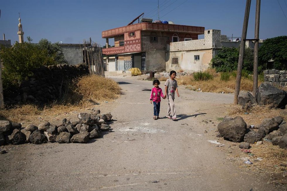 Archivo - Niños pequeños caminan entre grandes piedras colocadas a lo largo de una carretera principal en Abdín, en Quneitra, Siria. Los residentes bloquearon carreteras la noche anterior para detener una incursión de una patrulla militar israelí