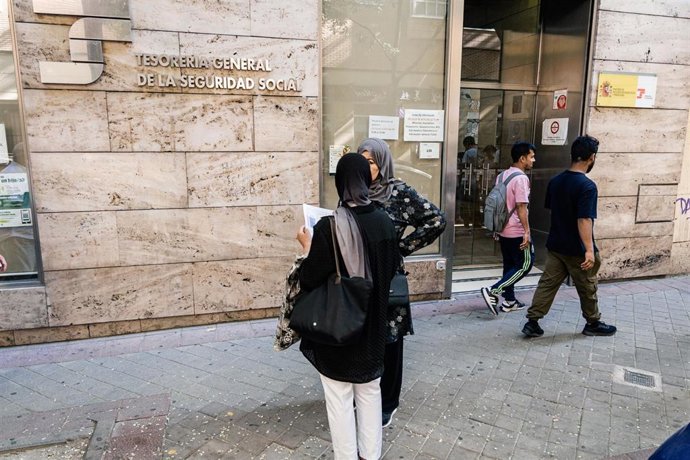 Varias personas migrantes esperan en el exterior de una oficina de la Seguridad Social