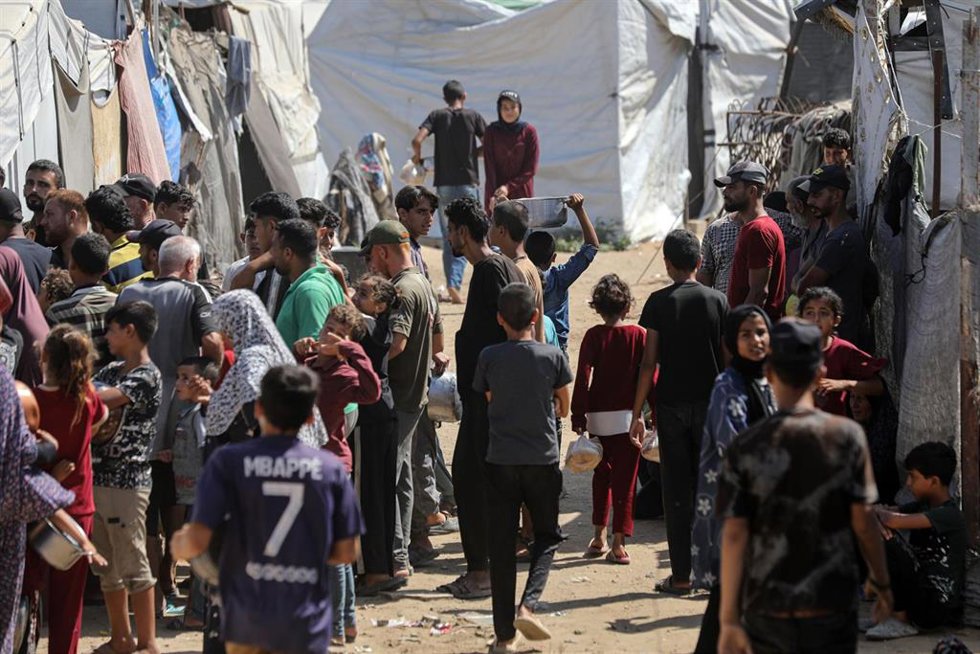 Los palestinos desplazados, entre ellos mujeres y niños, se reúnen para recibir comida en un punto de distribución de alimentos de una organización benéfica al este de la ciudad de Gaza.