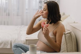 Archivo - Mujer embarazada comiendo un bollo. Fructosa