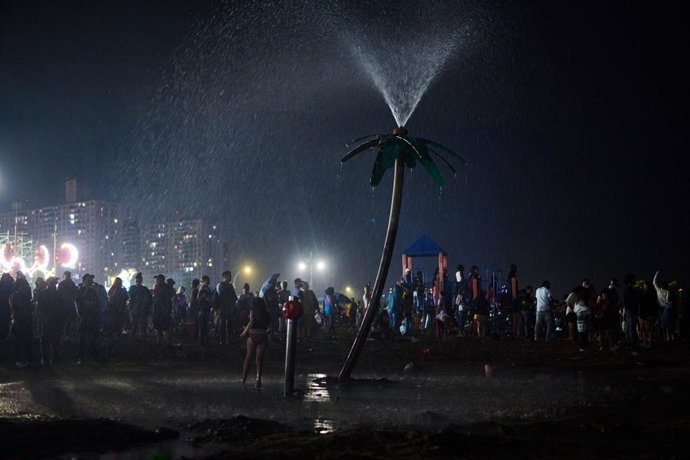 Archivo - July 4, 2024, New York, New York, USA: A young girl runs through the palm tree sprinkler on the beach at night in Coney Island on July 4th.