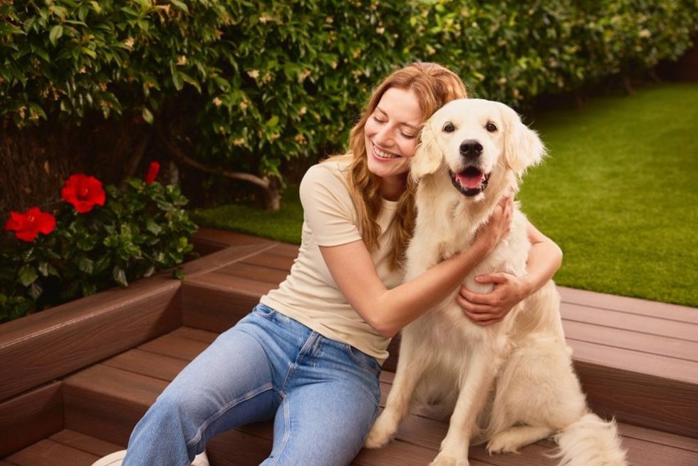Una mujer sentada junto a un perro en una zona ajardinada.