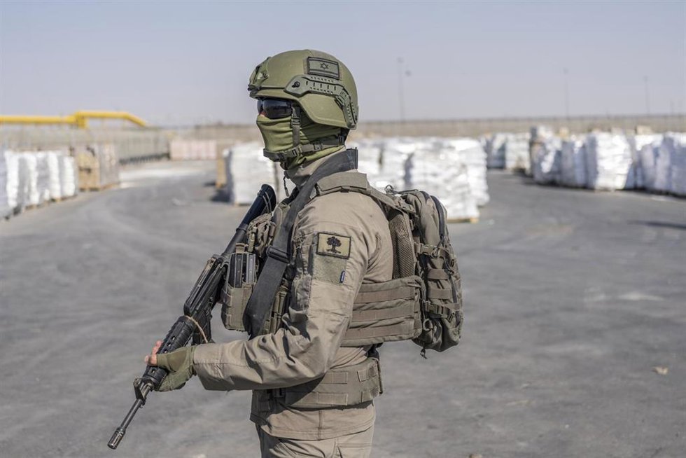 Archivo - Un soldado israelí se encuentra junto a unos paquetes de ayuda humanitaria que esperan ser recogidos en el lado palestino del paso fronterizo de Kerem Shalom.