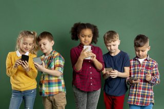 Archivo - Un grupo de niños utilizando teléfonos móviles.