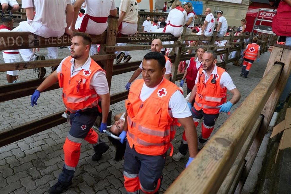 Voluntarios de Cruz Roja atienden a un herido en el quinto encierro de los Sanfermines 2026, con toros de José Escolar.