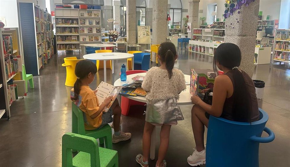 Las bibliotecas se convierten en refugios climáticos durante las horas de más calor. Una mujer lee libros junto a dos niñas en la biblioteca del centro Conde Duque.