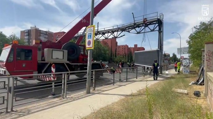 Bomberos de Madrid retiran un letrero luminoso dañado después de ser golpeado por un camión con la pluma desplegada