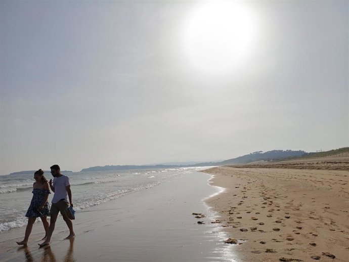 Dos personas pasean por la playa bajo el sol