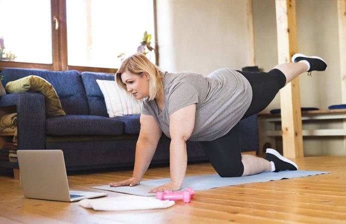 Archivo - Entrenamiento físico en línea para mujeres con sobrepeso que hacen ejercicio en casa, mirando la computadora portátil. Entrenamiento en la sala de estar.