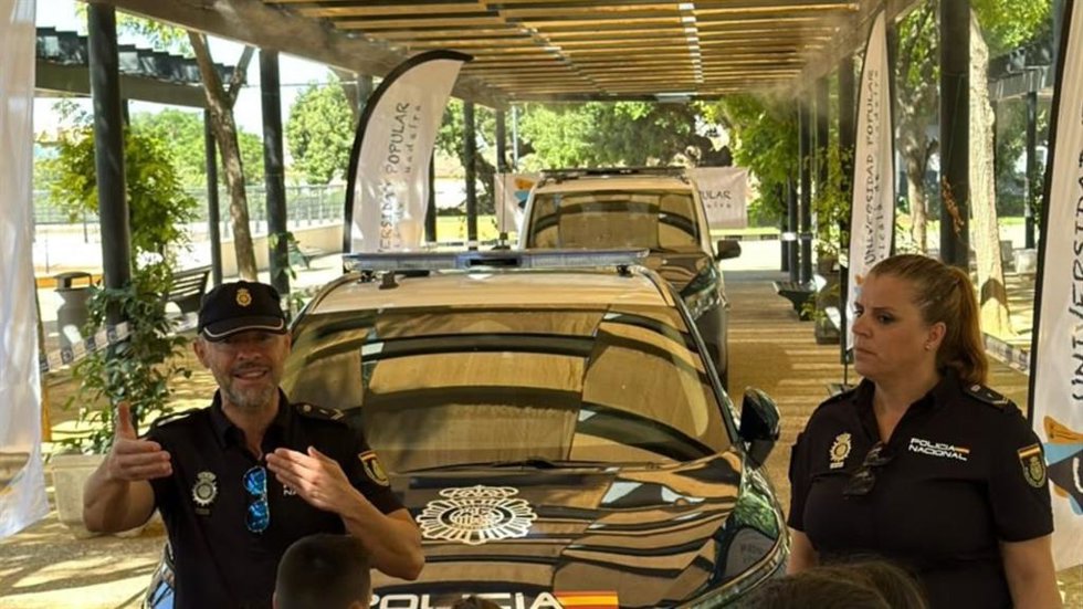 Dos agentes de la Policía Nacional muestran a los menores de los talleres de verano de la Universidad Popular de Alcalá de Guadaíra (Sevilla) los vehículos policiales.