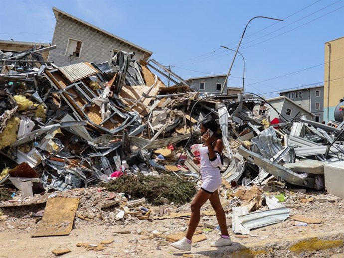 14 de julho de 2026, La Guaira, Venezuela: Uma mulher passa por um prédio desabado após os dois terremotos do mês passado, que causaram a morte de mais de 4.700 pessoas. Escavadeiras e trabalhadores da construção civil estão realizando operações de demoli