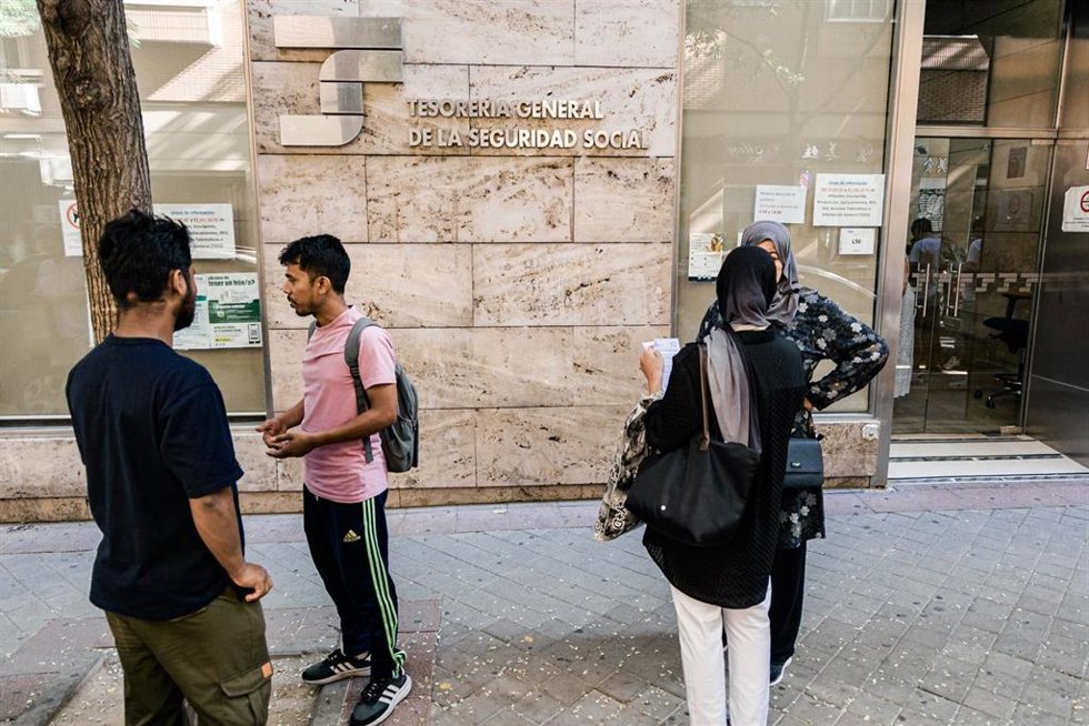 Varias personas migrantes esperan en el exterior de una oficina de la Seguridad Social.