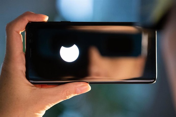 Archivo - 10 June 2021, North Rhine-Westphalia, Bielefeld: A person wearing SoFi glasses to protect him from the sun's strong rays is reflected in the display of a smartphone showing a small part of the sun is covered by the moon during the partial solar 