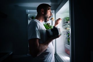 Archivo - Hombre comiendo por la noche mirando el refrigerador.
