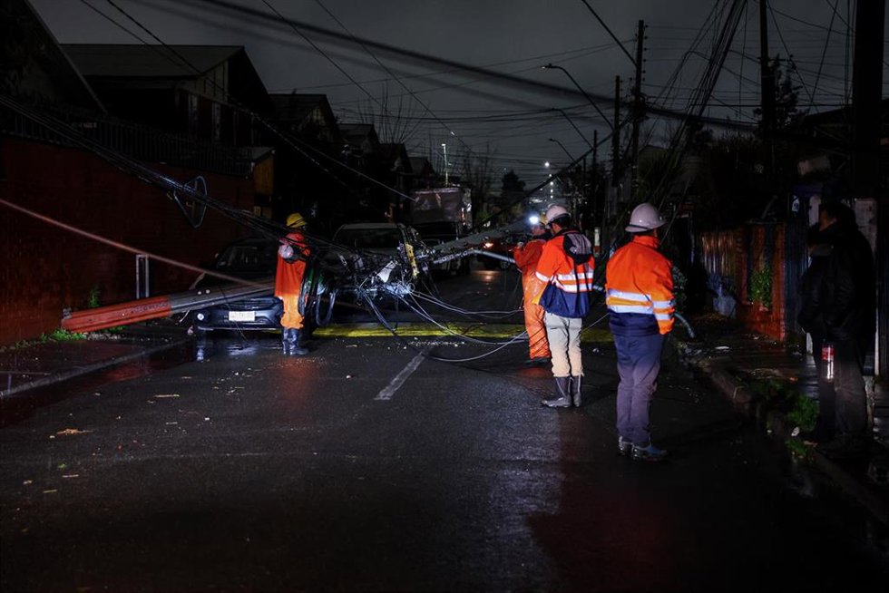  Unos trabajadores inspeccionan un poste eléctrico que se ha caído en plena calle, dejando a varias personas sin electricidad durante una tormenta que provocó inundaciones en algunas zonas de Santiago.