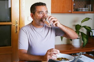 Archivo - Hombre bebiendo un vaso de agua durante la comida.