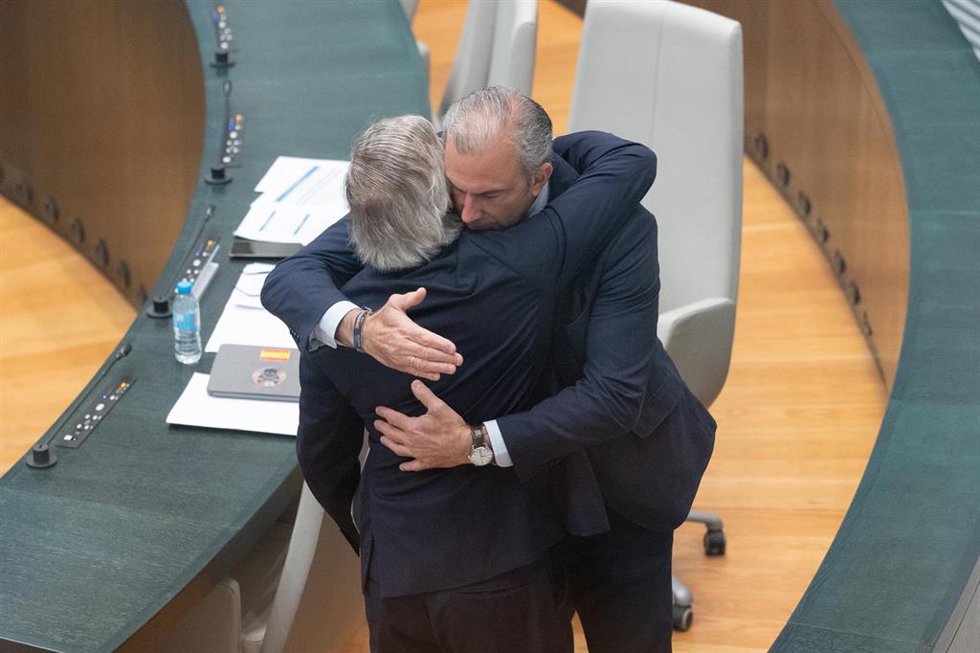 El que fuera secretario de vox en el Ayuntamiento, Ignacio Ansaldo Adriaensens, se abraza con el concejal no adscrito, Javier Ortega Smith (d), durante una sesión ordinaria del Pleno municipal, en el Palacio de Cibeles
