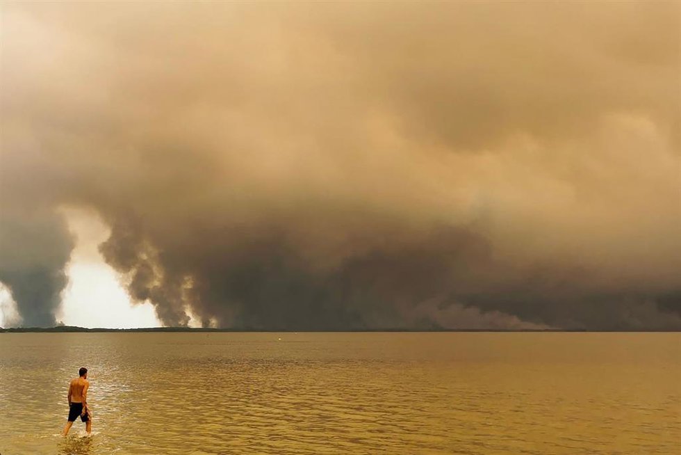 24 July 2026, France, Lacanau: A beachgoer walks along the Etang de Lacanau on Moutchic Beach in Lacanau, in southwestern France, as plumes of smoke from a forest fire rise into the sky. 