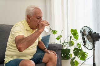 Archivo - Hombre refrescándose con un ventilador y bebiendo un vaso de agua en plena ola de calor.