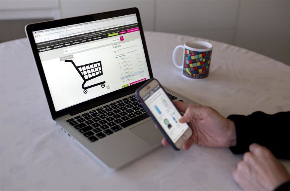 Archivo - Una persona compra con su teléfono móvil y ordenador 