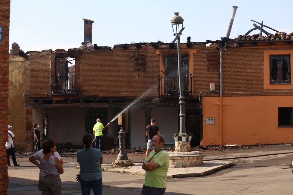 Varias personas enfriando con agua una de las dos casas quemadas durante un incendio forestal, a 30 de julio de 2026, en Castro del Condado, León, Castilla y León (España).