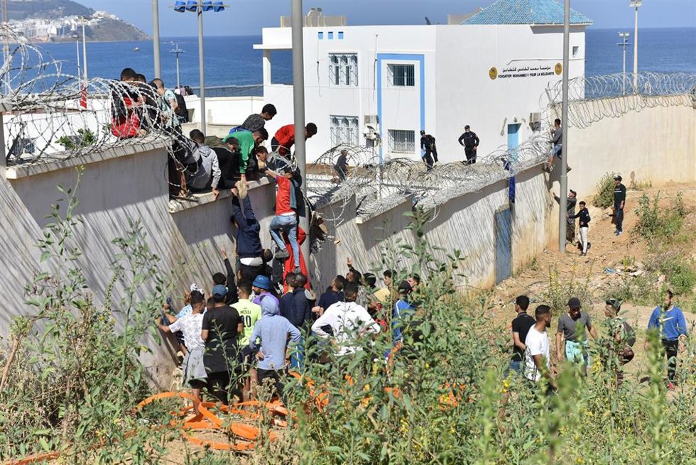Archivo - Migrantes trepan la valla fronteriza para entrar en el enclave español de Ceuta, en Fnideq (Marruecos), el 18 de mayo de 2021  