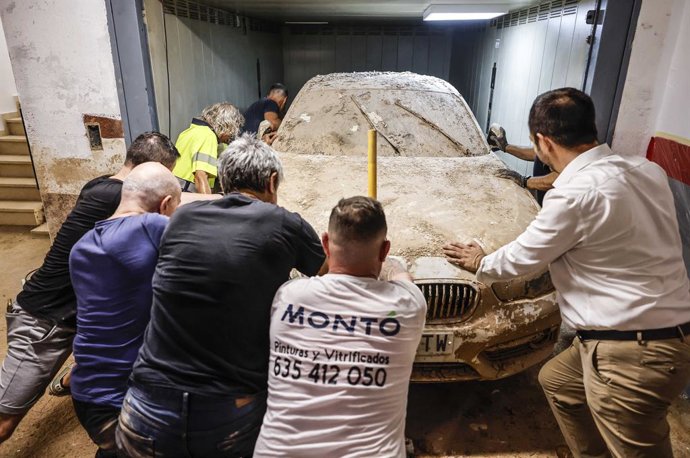 Diverses persones trauen un dels cotxes destrossats per la dana d'octubre del 2024 d'un garatge a Aldaia. 