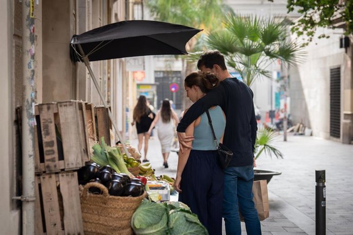 Archivo - Dos jóvenes se paran frente a una frutería en Barcelona
