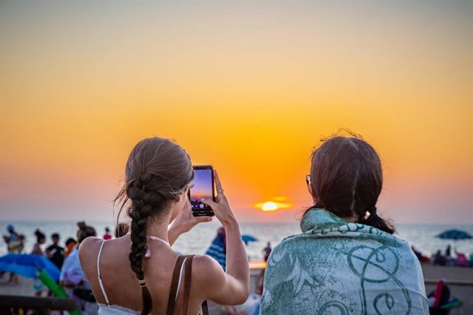 Dos jóvenes observan la puesta de sol en la playa de Camposoto, en San Fernando (Cádiz)