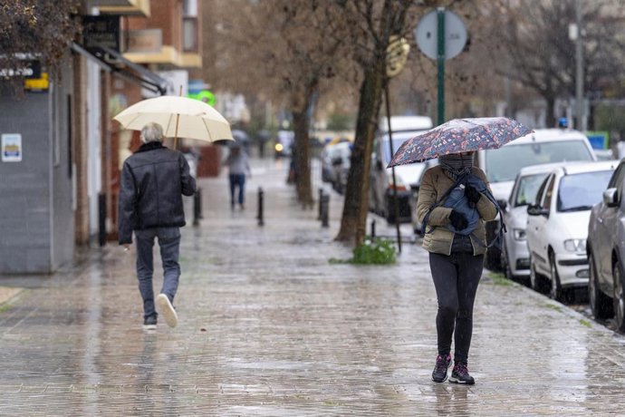 Archivo - Gente paseando se resguarda bajo un paragúa por la lluvia