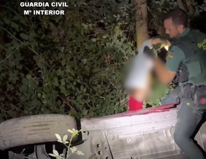 Momento en el que un guardia civil rescata a un niño de cuatro años que estaba en el interior de un coche suspendido entre la vegetación tras caer por un terraplén de 20 metros en Soportújar.