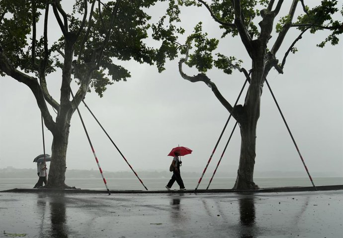 HANGZHOU, 9 de agosto de 2026  -- Visitantes passam por árvores temporariamente reforçadas ao longo do Lago Oeste, em Hangzhou, na província de Zhejiang, no leste da China, em 9 de agosto de 2026. O observatório nacional da China acionou, no domingo, um a