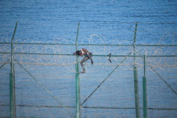 Archivo - Imagen de uno de los 153 migrantes entrando en Ceuta tras saltar la doble valla fronteriza, aferrado a las concertinas.