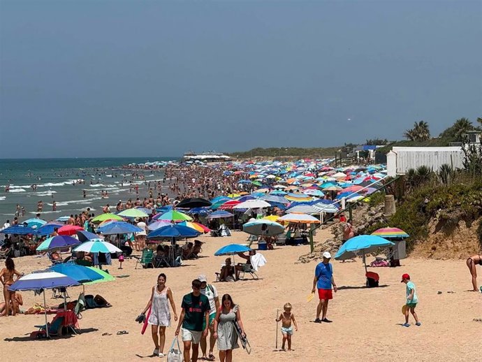 Imagen de una playa de Chipiona llena de sombrillas y bañistas este verano.