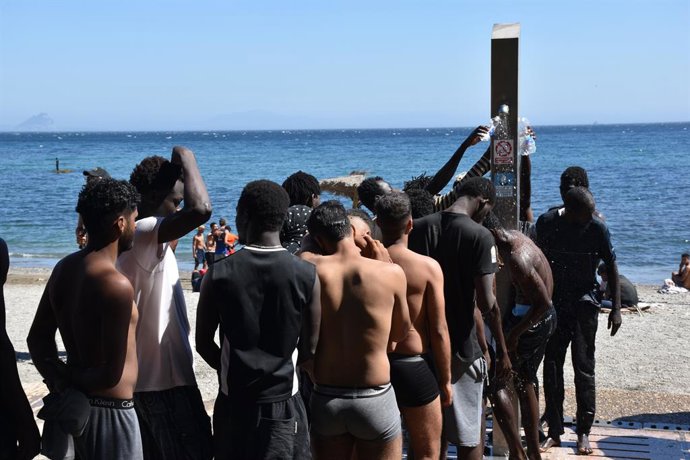 Várias pessoas tomam banho nos chuveiros públicos, na praia do Trampolín, em 5 de agosto de 2026, em Ceuta (Espanha). A Polícia Nacional iniciou o processo de triagem dos migrantes que permanecem em Ceuta, “cerca de 2.500”, segundo informações da De
