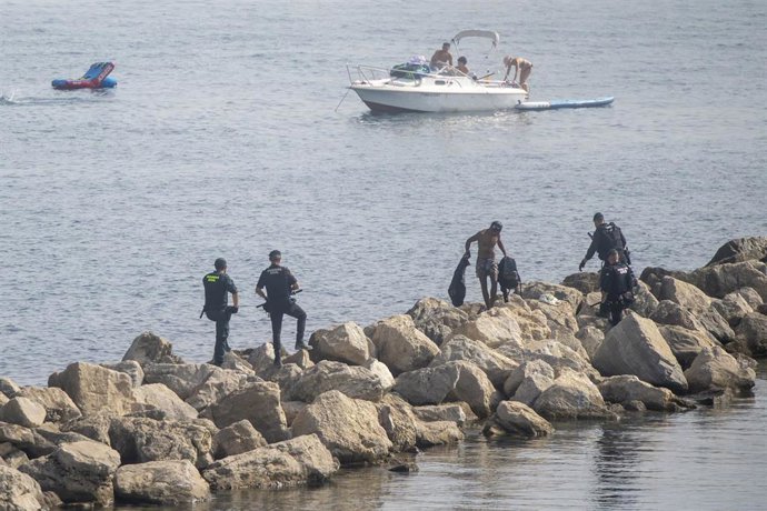 Varios migrantes, a 1 de agosto de 2026, en Ceuta (España) ante agentes de la Guardia Civil