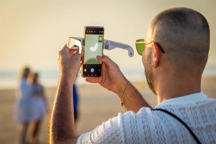 Una persona hace una foto del eclipse con su móvil en la playa de Camposoto en San Fernando (Cádiz)