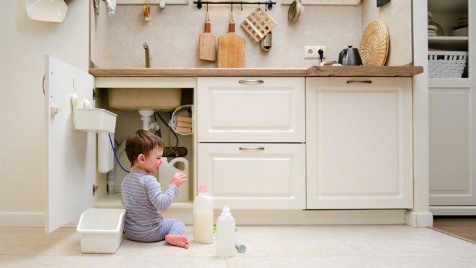 Archivo - Un niño está jugando con productos químicos de limpieza debajo del fregadero de la cocina. El bebé sostiene biberones con detergente. Niño de aproximadamente dos años (un año nueve meses)