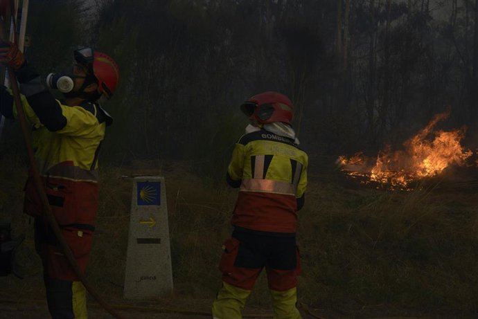 Dos bomberos durante las labores de extinción de un incendio forestal, la carretera nacional 525, a 15 de agosto de 2026, en O Riós, Ourense, Galicia (España).