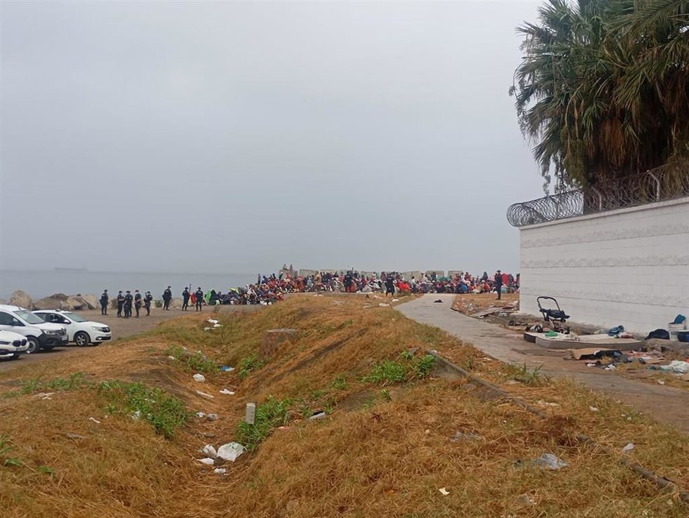 Migrantes aguardan en los alrededores de la playa de El Trampolín mientras los equipos de limpieza higienizan la zona