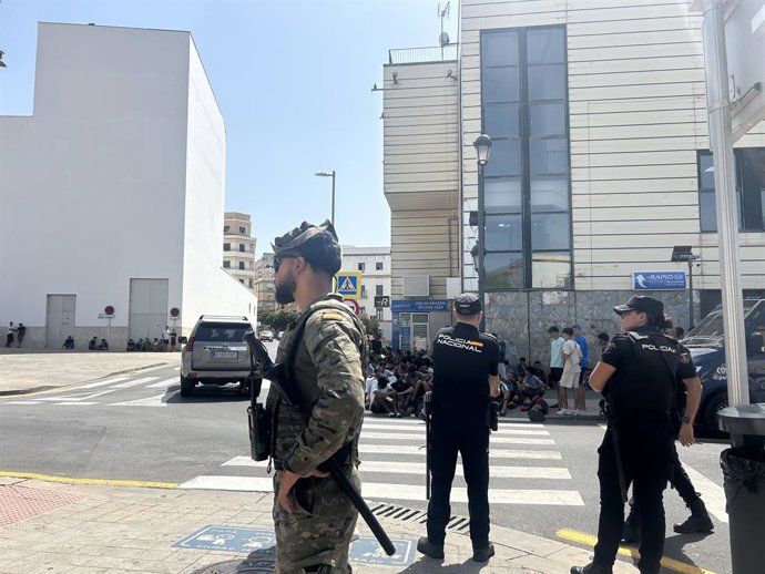 Vários militares prestam apoio aos agentes da Polícia Nacional ao lado de uma delegacia onde um grupo de menores aguarda para ter seus dados registrados, em 10 de agosto de 2026, em Ceuta (Espanha). A cidade acolhe milhares de pessoas que aguardam o retor