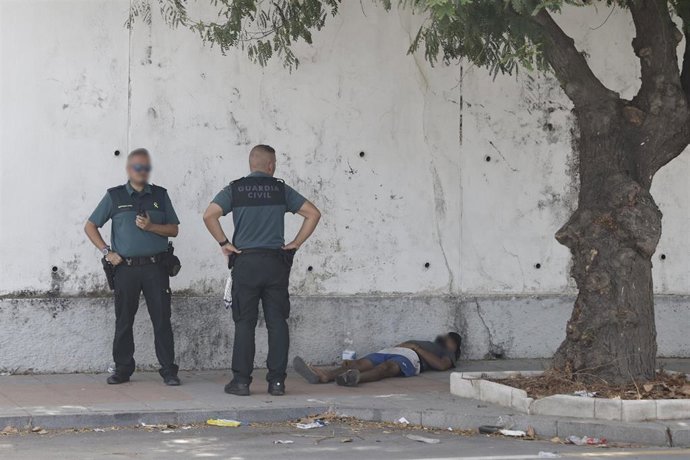 Dos agentes de la Guardia Civil observan a una persona tumbada, a 1 de agosto de 2026, en Ceuta (España). 