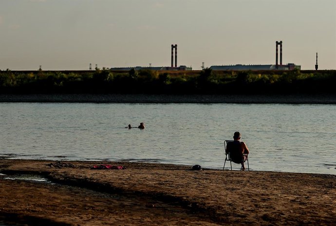 BUDAPEST, Aug. 3, 2026  -- A man sits on the bank of the Danube River, with the Paks nuclear power plant in the background, near Dunaszentbenedek, Hungary, Aug. 2, 2026. Hungary is entering its "most critical 5 days" as dropping water levels on the Danube