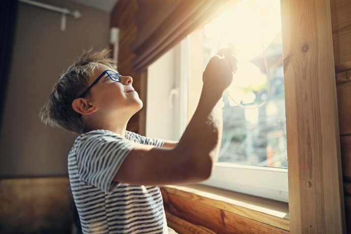 Archivo - Niño con gafas abriendo la persiana.