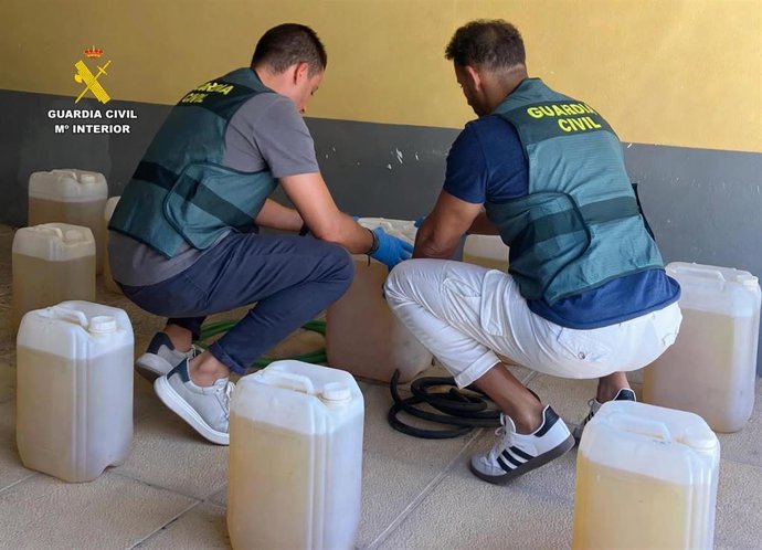 Dos agentes de la Guardia Civil junto a parte de las garrafas intervenidas