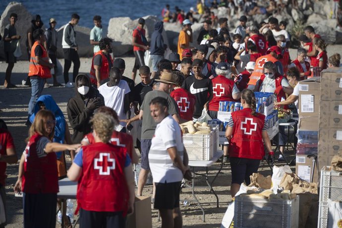 Membros da Cruz Vermelha distribuem comida aos imigrantes em uma praia, em 21 de agosto de 2026, em Ceuta (Espanha). Ceuta continua enfrentando uma grave crise humanitária após a histórica chegada em massa de mais de 70 mil migrantes, que atravessaram a n