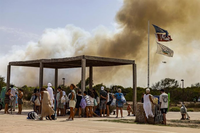 Várias pessoas evacuam a praia durante um incêndio florestal, em 27 de agosto de 2026, na Gola de Pujol, em El Saler, Valência, Comunidade Valenciana (Espanha). Três aeronaves e seis equipes do Corpo de Bombeiros Municipal de Valência trabalham no combate