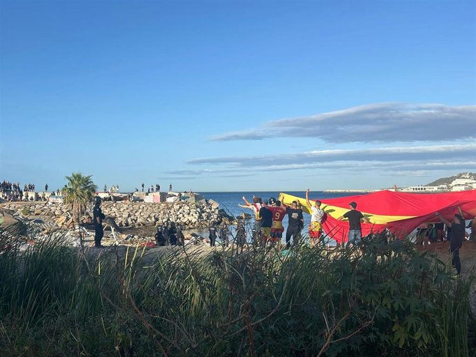Manifestantes con una bandera gigante de España en una playa de Ceuta