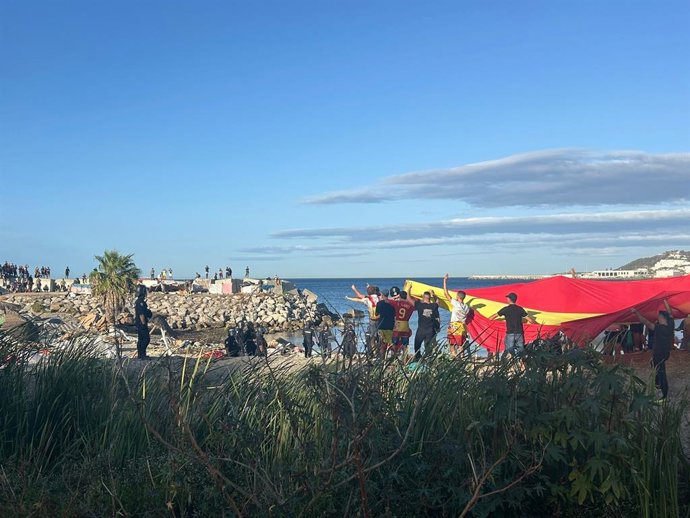 Manifestantes con una bandera gigante de España en una playa de Ceuta