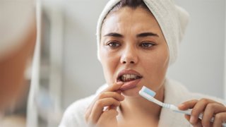 Archivo - Mujer mirándose al espejo preocupada mientras se cepilla los dientes.